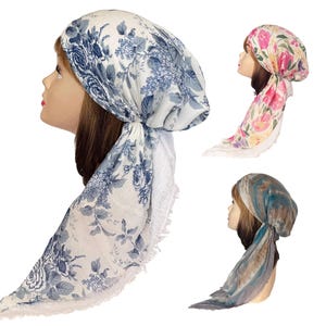 May include: Three headscarves on display. One is white with blue floral patterns and a lace trim. Another is pink with floral patterns. The third is a blue and brown tie-dye pattern. All are tied at the back.
