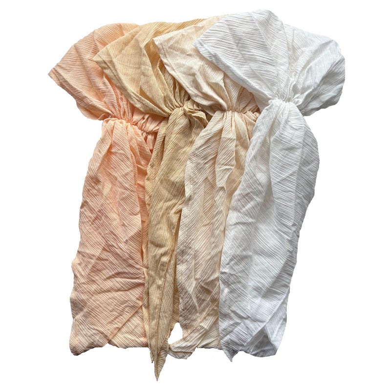 Puede incluir: Cuatro diademas de tela en tonos melocot&oacute;n, beige y blanco. Cada diadema est&aacute; fruncida en el centro y tiene lazos largos y fluidos. La tela tiene un aspecto texturizado y arrugado.