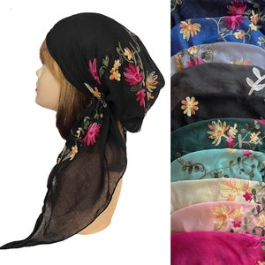 May include: A black sheer headscarf with floral embroidery in shades of pink, yellow, and green. The scarf is tied in a knot at the back of the head and flows down the back. The image also shows a variety of other colors of the same scarf.