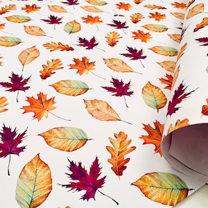 May include: White wrapping paper with a repeating pattern of red, orange, and yellow leaves. The leaves are in various shapes and sizes, and they are arranged in a random pattern.