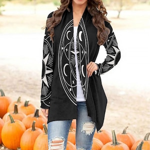Pode incluir: Cardigan preto com um design celestial branco com um sol, uma lua e estrelas. O cardigan tem uma abertura frontal longa e um caimento solto.