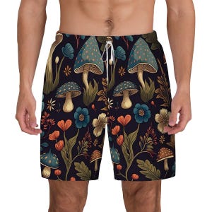 Puede incluir: Pantalones cortos de baño negros con un estampado colorido de setas, flores y follaje. El diseño presenta elementos turquesa, naranja y crema sobre un fondo oscuro. Los pantalones cortos tienen un cordón blanco.