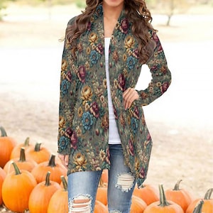 May include: A long, open-front cardigan featuring a floral design in green, yellow, blue, and burgundy. The cardigan is worn over a white top and paired with distressed blue jeans. Pumpkins are in the background.