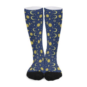 May include: A pair of knee-high socks with a celestial pattern. The socks feature a dark blue background with a repeating design of yellow suns, moons, and stars. The toes and heels are black, and the tops are white.