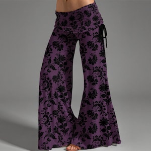 Può includere: Pantaloni palazzo viola con motivo floreale nero. Questi pantaloni a gamba larga hanno una vita alta arricciata e un dettaglio con coulisse sul lato. Il tessuto ha un aspetto morbido e fluido.