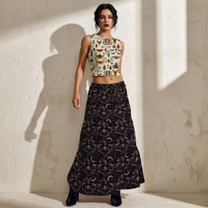 Op de afbeelding: Een vrouw draagt een tweedelige outfit. De top is een crèmekleurige crop top met een patroon van verschillende insecten. De lange rok is zwart met een herhalend patroon van manen, motten en bloemen.