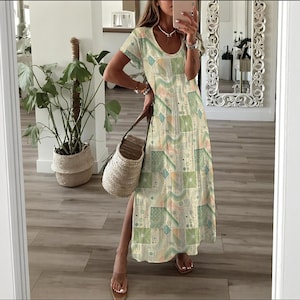 May include: A long, flowing dress with a geometric pattern in shades of green, blue, and peach. The dress has short sleeves and a scoop neckline. A woven tote bag is held in the hand. The dress has a side slit.