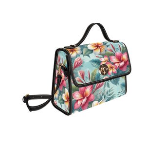 Op de afbeelding: Handtas met bloemenprint met een zwart handvat en riem. De tas heeft een lichtblauwe achtergrond met roze, gele en witte bloemen. De tas heeft een gouden sluiting en zwarte rand.