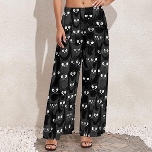 Könnte beinhalten: Schwarze weite Hose mit einem schwarzen Katzenmuster. Die Katzen haben weiße Augen und wiederholen sich auf der gesamten Hose.