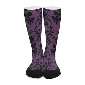 Könnte beinhalten: Ein Paar kniehohe Socken mit lila Hintergrund und schwarzem Blumenmuster. Die Socken haben schwarze Zehen und weiße Oberteile. Das florale Design umfasst stilisierte Blumen und Blätter.