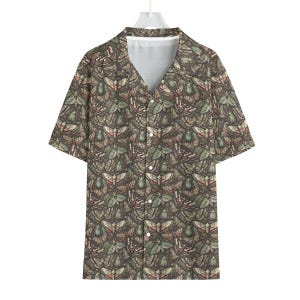 Può includere: Camicia a maniche corte con scollo a V. La camicia presenta un motivo ripetuto di varie falene e insetti nelle tonalità del marrone, verde e beige. La camicia è appesa a una gruccia bianca.