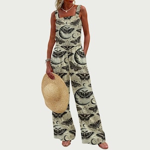 May include: Cream-coloured jumpsuit featuring a repeating pattern of moths, moons, and stars. The jumpsuit has wide straps, a square neckline, and wide-leg trousers. A straw hat is held in the hand. The overall style is bohemian.