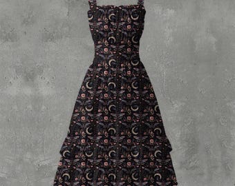 May include: A black dress with a floral and crescent moon pattern. The dress has a square neckline, wide straps, and a tiered skirt. The pattern includes pink flowers and moth illustrations.