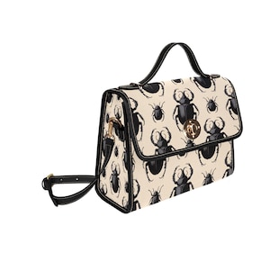 Könnte beinhalten: Cremefarbene Handtasche mit schwarzem Käfermuster. Die Tasche hat einen schwarzen Griff und Riemen mit goldfarbener Hardware. Der Klappenverschluss hat einen goldfarbenen Verschluss. Ein stilvolles Accessoire.