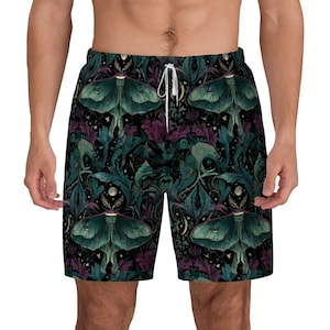 Puede incluir: Pantalones cortos oscuros con un patrón repetido de polillas verdes, hojas moradas y lunas sobre un fondo negro. Los pantalones cortos tienen un cordón blanco y están hechos de un material suave y cómodo.