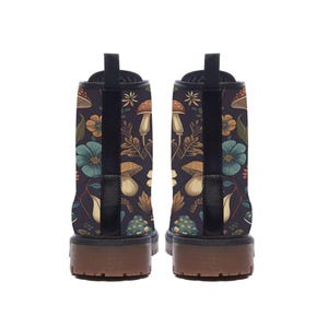 The back view of two black ankle boots showcasing their chunky brown lug soles and the continuous mushroom and flower pattern.