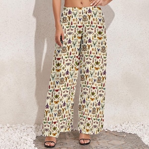 May include: Wide-leg pants with a cream background and a repeating pattern of colorful insects. The insects include butterflies, beetles, and other bugs in shades of red, green, purple, and brown. The pants are worn with black sandals.