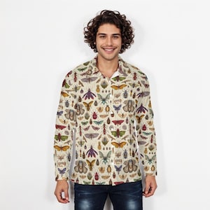 Pode incluir: Camisa bege com botões com um padrão detalhado de insetos em várias cores. A camisa de manga comprida apresenta uma colagem de borboletas, besouros e outros insetos. A camisa é usada por uma pessoa com cabelo encaracolado escuro e jeans azuis.