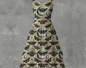 May include: A cream-colored dress with a black moth and moon pattern. The dress features a square neckline, wide straps, and a flared skirt. The design includes crescent moons, stars, and detailed moth illustrations, creating a gothic or celestial theme.