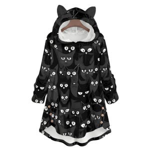 May include: Black hooded blanket with a repeating pattern of black cat faces with white eyes and whiskers. The hood has cat ears. The interior lining is white. The blanket has long sleeves and a rounded hem.