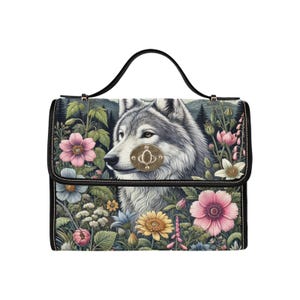 Può includere: Una borsa a mano in pelle nera con una stampa di lupo e fiori. Il lupo è grigio e bianco ed è circondato da fiori rosa, gialli e bianchi.