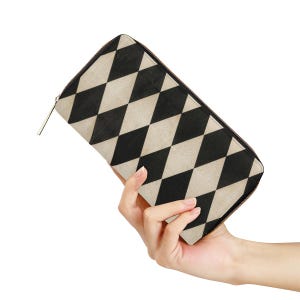 May include: A rectangular wallet featuring a repeating black and beige diamond harlequin pattern across the exterior surface. The wallet is secured with a dark zip that runs along the top and side edges, finished with a simple metal zip pull.