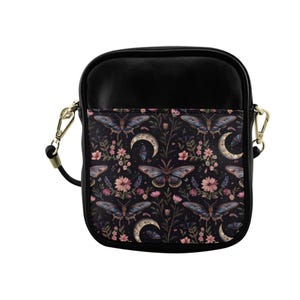 Può includere: Borsa a tracolla nera con patta con un motivo floreale scuro con falene, lune e fiori. La borsa ha una tracolla nera e hardware color oro. La borsa misura circa 20 cm di larghezza e 23 cm di altezza.