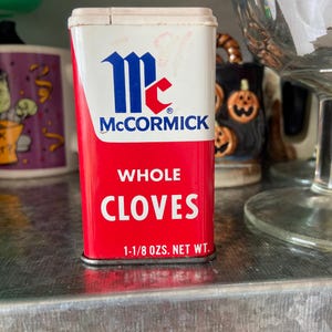 May include: A red and white metal tin of McCormick Whole Cloves. The tin has a blue and red logo with the text "McCormick" and the words "Whole Cloves" in white letters. The tin is 1-1/8 oz. net weight.