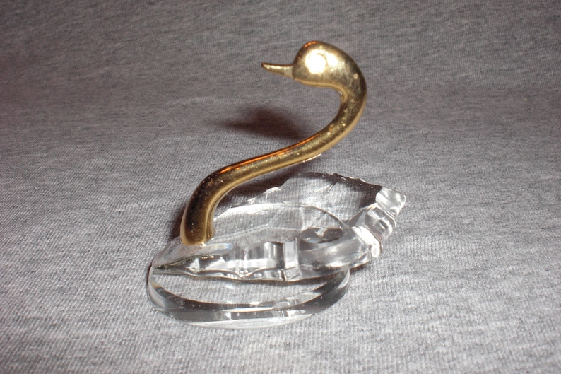 May include: A crystal swan ring holder with a gold-tone neck and head. The swan is sitting on a clear crystal base.