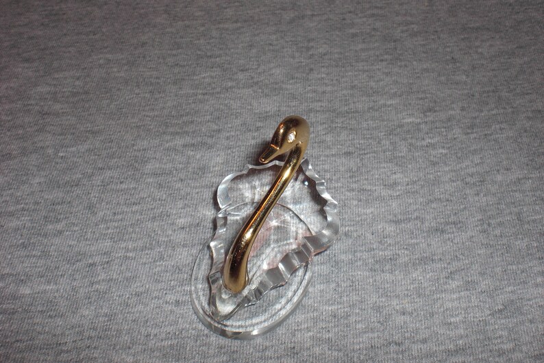 May include: A crystal swan figurine with a gold-plated neck and head. The swan is perched on a crystal base.