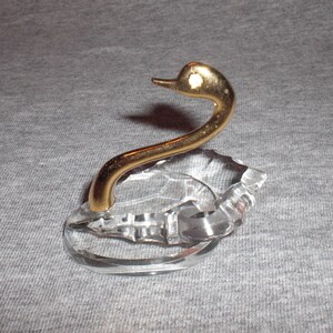 May include: A crystal swan ring holder with a gold-tone neck and head. The swan is perched on a clear crystal base.