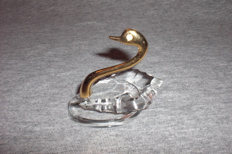 May include: A crystal swan ring holder with a gold-tone neck and head. The swan is perched on a clear crystal base.