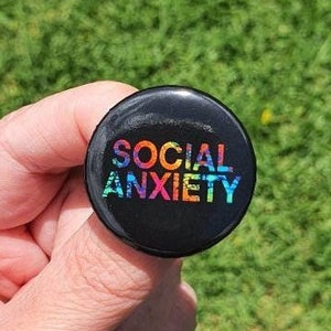 May include: A black button with the words "SOCIAL ANXIETY" in rainbow colours.