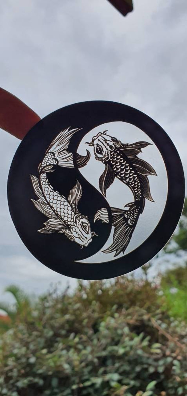 May include: A black and white Yin and Yang design featuring two koi fish. The fish are intricately detailed with scales and fins, set against a cloudy sky background. The artwork is circular.