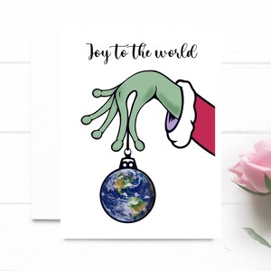 Alegría para el mundo. Mano alienígena que sostiene el adorno de Navidad de la Tierra. Tarjeta de vacaciones. Tarjeta de Navidad divertida.