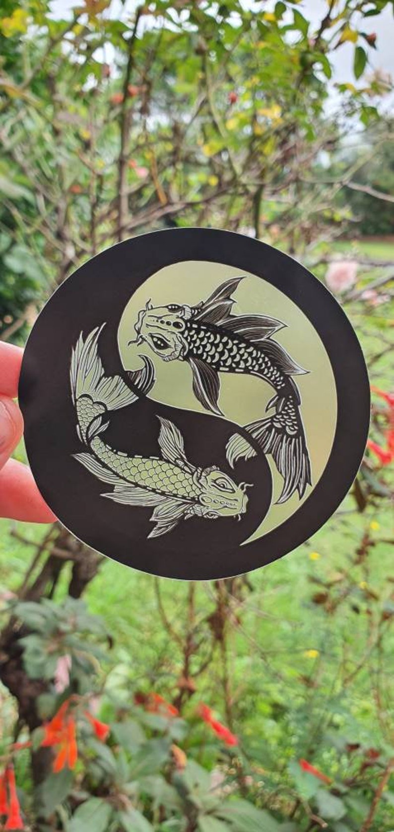 May include: A round black sticker featuring a Yin and Yang design with two koi fish. The fish are detailed with scales and fins, set against a light green background.