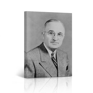 May include: Black and white portrait photograph of a man wearing a suit and tie. He is wearing glasses and has a serious expression on his face.