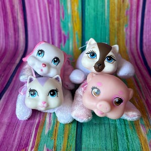 May include: Four plush animal toys with plastic faces. One is a white cat with purple accents, one is a white dog with pink ears, one is a white and brown cat with blue eyes, and one is a pink pig with brown eyes. All have soft bodies.
