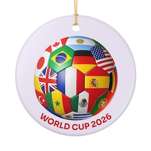 Op de afbeelding: Een ronde, witte keramische ornament met een voetbalontwerp bestaande uit verschillende nationale vlaggen, waaronder de Nederlandse vlag, Brazilië en Frankrijk. De tekst "WORLD CUP 2026" is in het rood gedrukt.