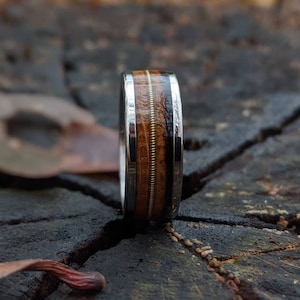 Puede incluir: Un anillo de madera con una banda plateada y una banda delgada de oro. La madera es de color marrón oscuro con una veta marrón clara.