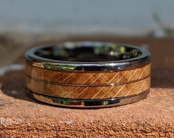Puede incluir: Un anillo de plata y madera con un patrón de veta de madera. El anillo tiene una banda de plata pulida y una incrustación de madera.
