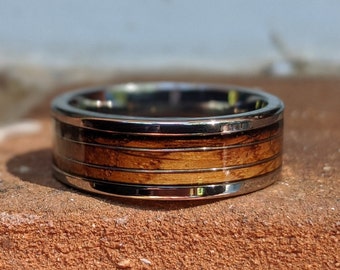 May include: A silver and wood ring with a brown wood inlay. The ring has a polished silver finish and a smooth wood surface.