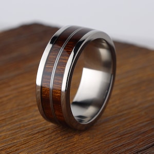 May include: A titanium ring with a brown wood inlay. The ring has a polished finish and a bevelled edge.