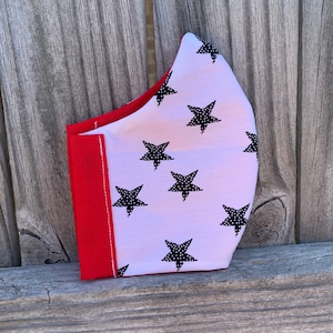 Op de afbeelding: Een wit mondkapje met een rode rand en een patroon van zwarte sterren. De sterren zijn gevuld met kleine witte stippen.