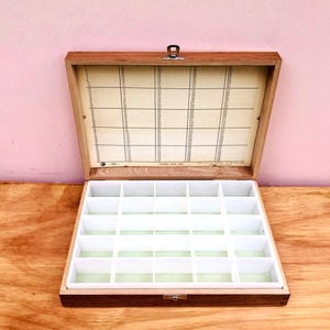 May include: A rectangular wooden storage box with a hinged lid and a metal latch. The interior features a white grid with twenty-four compartments. The inside of the lid displays a printed reference chart with numbered rows and columns.