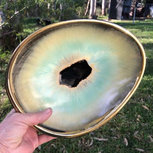 May include: An oval ceramic bowl featuring a gradient glaze that transitions from a dark brown rim to a soft mint green and cream centre, surrounding a deep, irregular black cavity at the base with a smooth, reflective finish throughout.