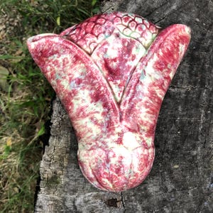 May include: A wall-mounted ceramic planter featuring a triangular, tulip-like shape with a glossy finish. The surface displays a mottled pattern of deep crimson red, soft cream, and pale green hues, with a textured, scale-like design at the top.