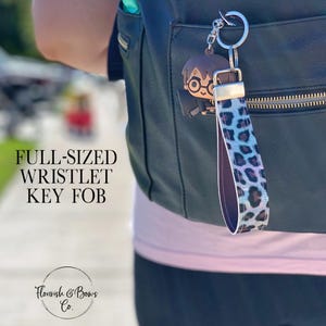 May include: A full-sized wristlet key fob with a leopard print strap in shades of blue, purple, and black. The key fob features a silver-tone keyring and a Harry Potter-themed charm. The text "FULL-SIZED WRISTLET KEY FOB" is visible.