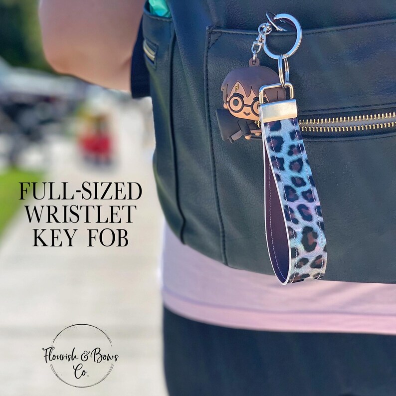 May include: A full-sized wristlet key fob with a leopard print strap in shades of blue, purple, and black. The key fob features a silver-tone keyring and a Harry Potter-themed charm. The text "FULL-SIZED WRISTLET KEY FOB" is visible.