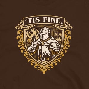 Op de afbeelding: Bruin t-shirt met een gouden en witte afbeelding van een ridder die een duim omhoog geeft, met de tekst "'TIS FINE". Het ontwerp staat in een schildvormige vorm, met vlammen. Het t-shirt is van Dungeon Arsenal.